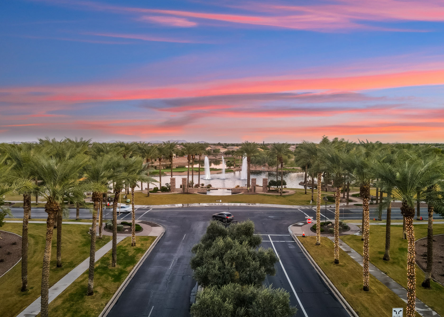 A road with palm trees and a building in the background.