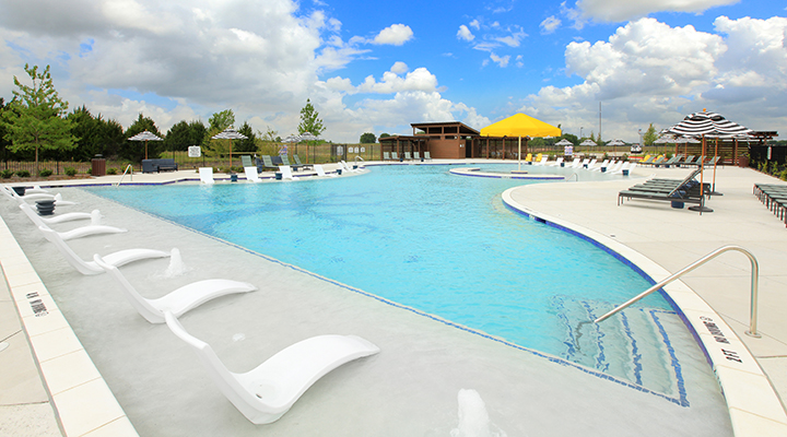 A pool with a lounge chair and umbrellas by it.