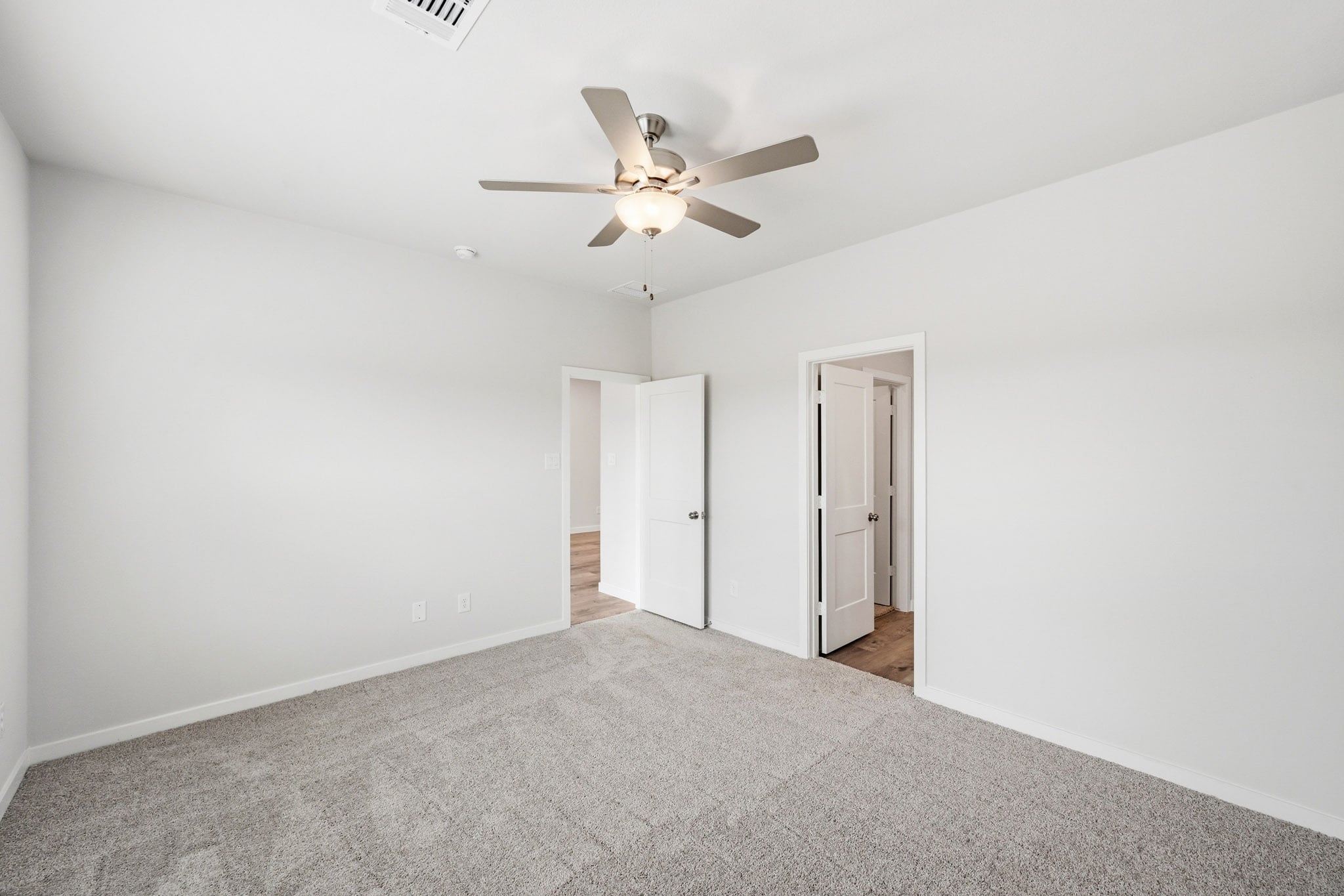 A room with a ceiling fan and a carpet.